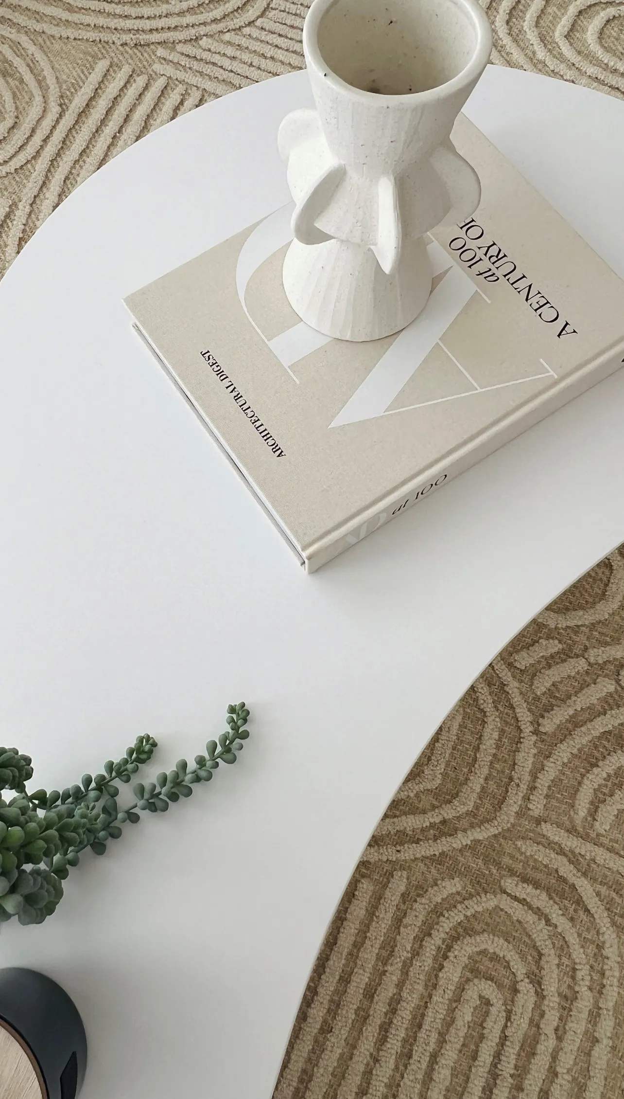 White organic coffee table with sculptural vase and architecture book on textured rug